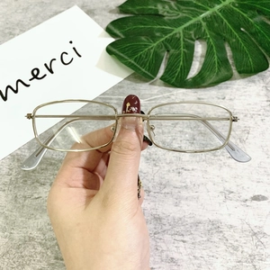 Detail of vintage metal square sunglasses frame held against a minimalist background