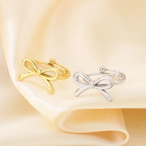 Detailed comparison of gold and silver bow rings on champagne silk fabric background