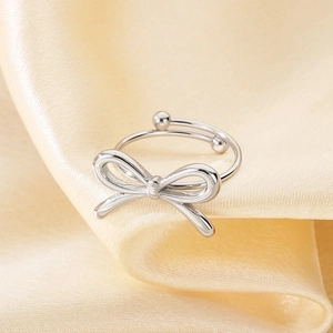 Macro detail of silver bow-shaped adjustable ring on elegant silk fabric background