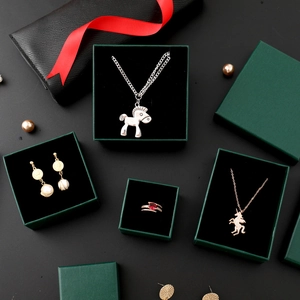 Dark green jewelry boxes with horse pendants, ruby rings and pearl earrings on black