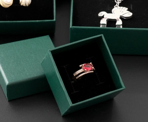 Detail view of dark green textured jewelry box with black velvet lining and ruby ring