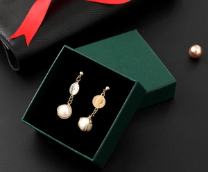 Detail of gold coin earrings with white pearls inside a dark green velvet jewelry gift box