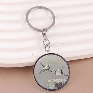 Close-up of a silver keychain with a round pendant featuring cranes and pine trees