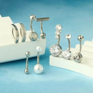 9-piece stainless steel belly ring set with cubic zirconia and pearls on blue background