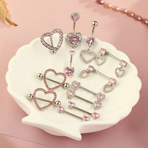 Pink heart-shaped zircon belly rings and nipple piercings on a white shell tray