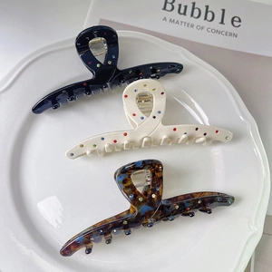 Three acetate hair claws in black, white, and tortoiseshell with colorful rhinestones