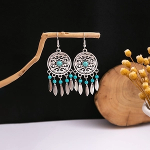 Detail of bohemian turquoise drop earrings with hollow floral design on a wooden branch