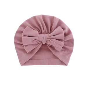 Soft dusty pink baby turban hat with a large bow decoration on white background