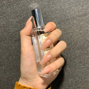 Glänzende nude-rosa Ballerina-Kunstnägel an einer Parfümflasche auf grauem Hintergrund