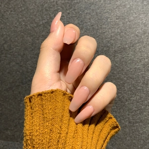 Glänzende, nudefarbene Press-on-Nägel in Sargform an einem Modell mit gelbem Pullover
