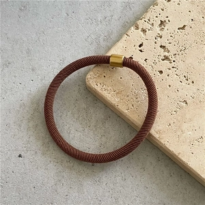 Detail of a brown woven elastic hair tie with a gold metal fastener on a stone base