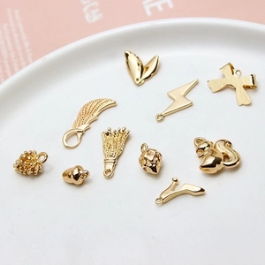 Golden DIY metal charms set with wings and pinecones on a white ceramic plate