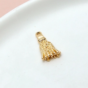 Macro shot of a shiny golden metal tassel pendant for DIY jewelry making on white ceramic