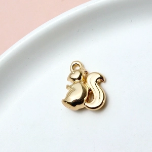 Close-up of a golden squirrel-shaped pendant charm on a white plate with pink background