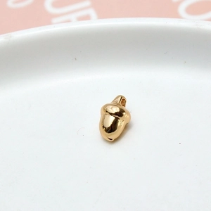 Macro view of a golden acorn-shaped pendant in a white ceramic dish for DIY jewelry making