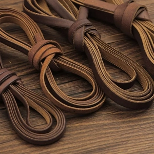 Detailed close-up of brown flat leather cords for DIY crafts on dark wood background