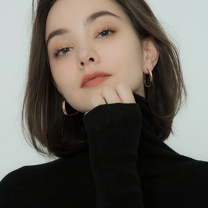 Close-up of golden irregular textured square hoop earrings worn by a female model