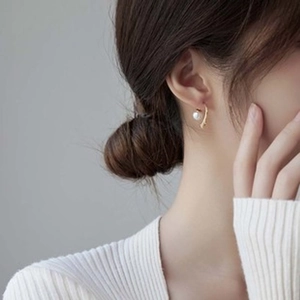 Close-up of elegant gold curved hoop earring with a white pearl on a female model