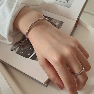 Detail shot of a silver twisted bangle and minimalist ring styled on an open book