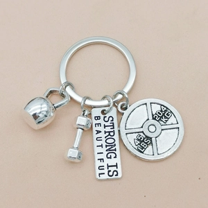 Detail of silver fitness keychain with kettlebell, dumbbell and Strong Is Beautiful tag