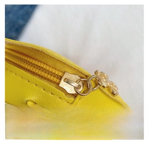 Detailed close-up of smooth gold metal zipper on a bright yellow leather mini bag