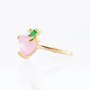 Macro shot of gold-plated ring with pink peach crystal and small green leaf stone