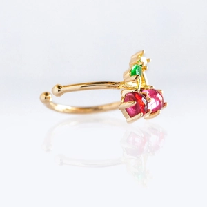 Macro shot of gold cherry ring with red and green gemstones on white background
