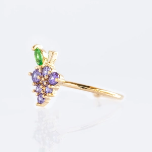 Macro detail of a gold ring featuring purple zircon grapes and green leaf accents
