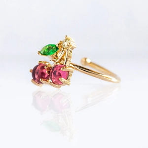 Macro shot of gold cherry ring with red crystal fruits and green leaf on white base