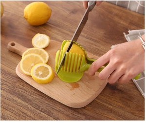Handheld green slicer tool cutting lemon slices on a wooden board in a kitchen setting