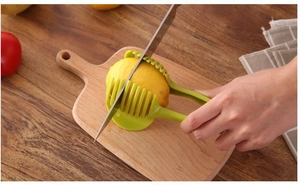 Green plastic slicer tool holding a lemon for uniform cutting on a wooden board