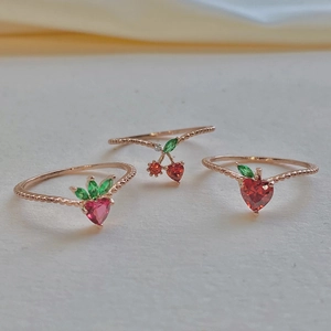 Rose gold rings featuring red heart-shaped crystals and green leaves in a cluster