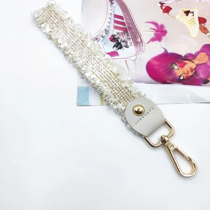 Detail of off-white lace fringe strap with white leather and gold metal lobster clasp