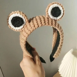 Nahaufnahme des handgestrickten khakifarbenen Stirnbands mit großen Cartoon-Froschaugen