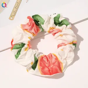 Close-up of a white fabric scrunchie with red strawberry print and pleat details