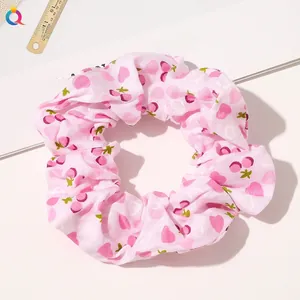 Close-up of pink scrunchie with sweet cherry and heart patterns in a pleated fabric design
