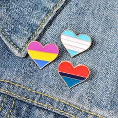Three heart enamel pins in pride flag colors on a blue denim background with gold plating