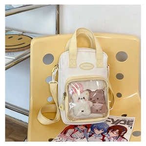 Detail of a beige canvas Ita bag with a clear PVC front pocket and cute bear plush charm