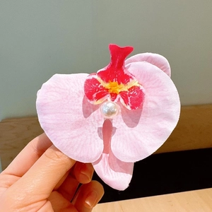Detail of pink orchid hair clip with central pearl bead held in hand close-up