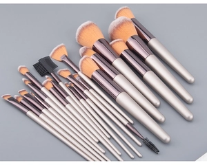 Flat lay of 18 champagne makeup brushes with dual-tone bristles on a grey surface