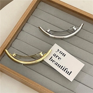 Minimalist metallic curved hair clips in gold and silver finish on velvet display tray