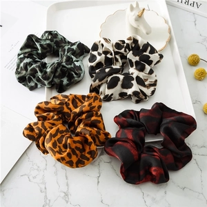 Four leopard print satin scrunchies in various colors displayed on a luxury marble surface