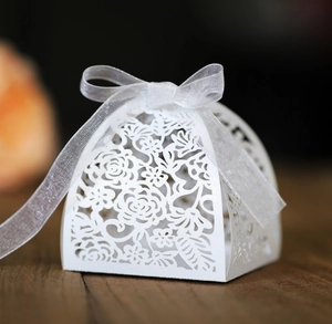 Close-up of white laser-cut floral wedding candy box with an elegant white silk ribbon bow