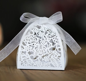 Detail of white laser-cut hollow candy box with floral patterns and a silk ribbon bow
