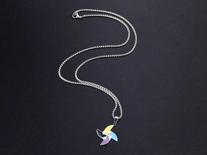 Macro detail of silver necklace featuring a colorful enamel windmill pendant on black backdrop