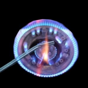 Heat-resistant glass drinking straw being tested over a gas stove flame close-up