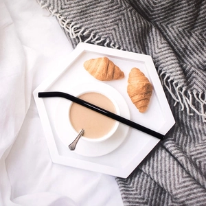 Close-up of a reusable black curved glass straw on a coffee cup in a cozy breakfast setting