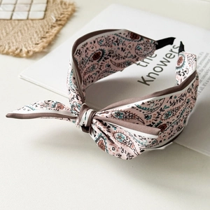 Detail of a pink paisley satin headband with a stylish top knot on a white desk