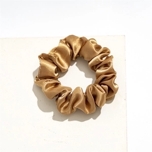 Close-up of golden satin scrunchie showing smooth silk texture and pleated design details