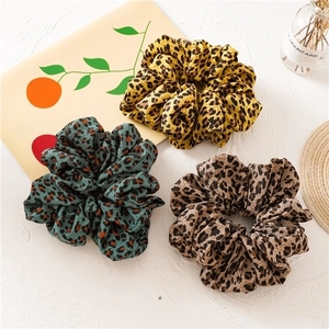 Three large leopard print hair scrunchies in yellow, green and brown fabric on white background